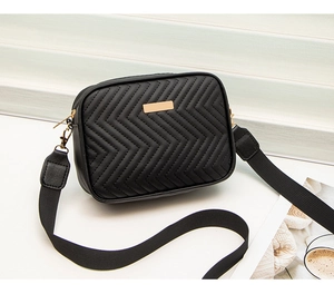 Detail of black quilted camera bag with golden metal plate and wide nylon shoulder strap