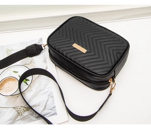Detail of black quilted camera bag featuring golden zipper and wide nylon strap on white background