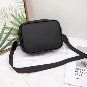 Minimalist black square crossbody bag with adjustable strap on white fabric background
