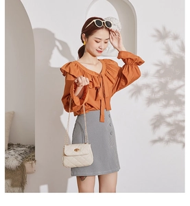 Close-up of a white quilted chain crossbody bag paired with an orange ruffle shirt