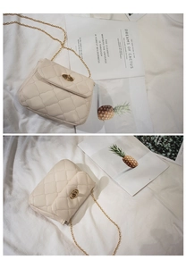 Detailed view of cream quilted crossbody bag with gold twist lock on a textured fabric