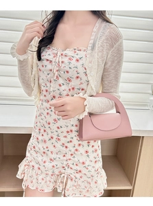 Détail du sac à main rose en cuir grainé avec poignée courbée sur robe fleurie