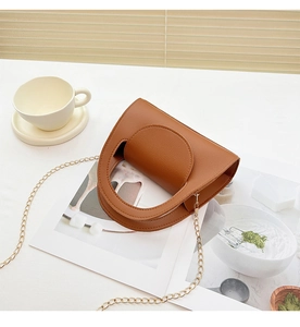 Sac à main en cuir marron avec poignée découpée et chaîne dorée sur table blanche