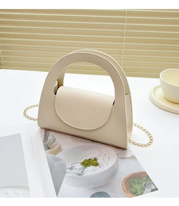 Détail d'un sac à main en cuir crème avec bandoulière chaîne dorée sous une lumière douce