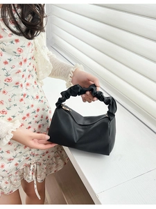 Close-up of black lychee leather handbag with pleated handle and golden zipper detail