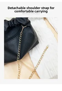 Close-up of black lychee grain leather pillow bag with detachable gold chain strap