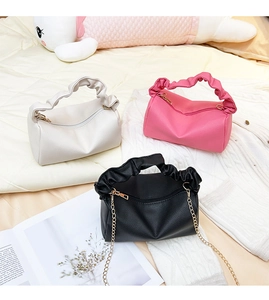 Close-up of pleated leather handbags in white, pink, and black with gold chain straps