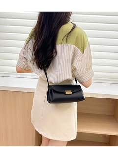 Detail of black litchi grain crossbody bag with gold buckle on a model's shoulder
