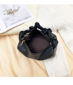 Top view of black lychee-textured pillow bag with pleated handle on silk background