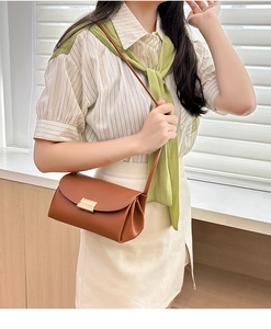 Detail of brown litchi grain leather crossbody bag featuring a gold metal lock and pleats