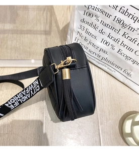 Close-up of black quilted camera bag with gold zipper and letter print strap