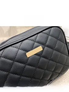 Close-up of black quilted leather camera bag featuring gold metal plate and zipper detail
