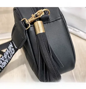 Macro view of black quilted camera bag with golden hardware and long tassel charm detail