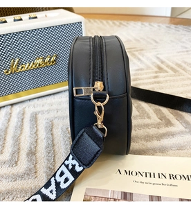 Detail of round black crossbody bag with golden metal zipper and lettered strap