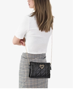 Model wearing a black quilted crossbody bag with gold heart clasp and chain strap