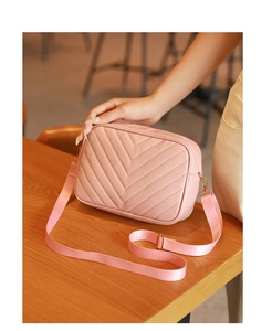 Detalle de bolso tipo cámara rosa con costuras en V y correa sobre superficie de madera