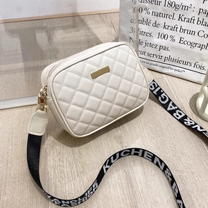 Detail view of cream quilted crossbody bag with stylish wide woven strap on wood floor