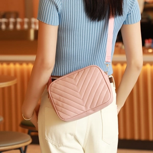 Bolso rosa con acolchado en V y correa ancha de tela llevado por una modelo en un café
