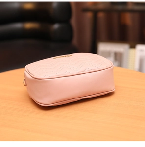Détail d'un sac rose avec surpiqûres en V et logo doré sur une table en bois naturel