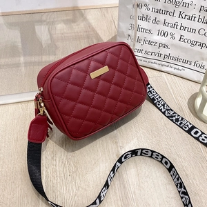 Close-up of wine red quilted crossbody bag with golden hardware and wide jacquard strap