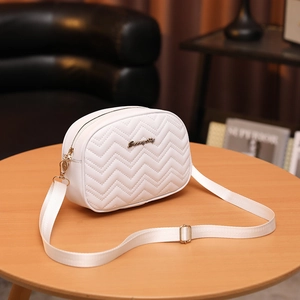 Sac bandoulière blanc matelassé avec logo doré et sangle réglable sur une table en bois