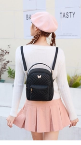 Close-up of a black quilted mini backpack featuring a gold butterfly buckle decoration