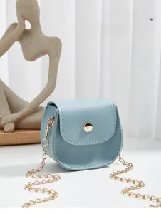 Detail of light blue faux leather saddle bag with gold chain and round metallic snap closure
