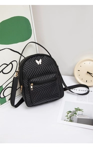 Close-up of black quilted backpack with golden butterfly logo in a lifestyle setting