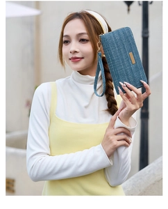 Detail of navy blue herringbone fabric clutch bag with gold logo plate and wrist strap