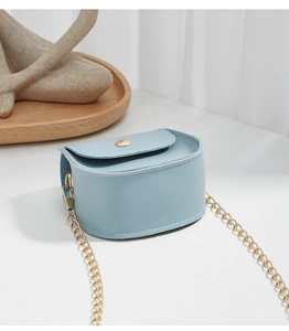 Detail of light blue mini crossbody bag with gold chain and circular metal clasp on a tray