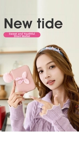 Pink polka dot bow mini wallet with plush ball pendant held by a model in a cozy setting
