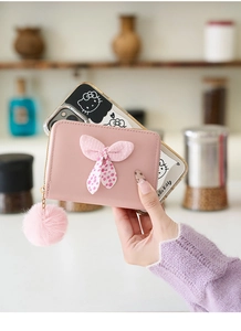 Detail of pink mini wallet with polka dot bow and fluffy ball charm accessory