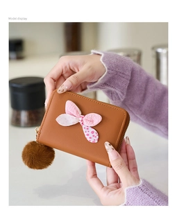 Detail of a brown mini wallet featuring a polka dot bow and a fluffy pom-pom pendant