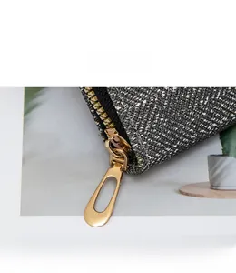 Close-up of golden teardrop zipper pull on grey textured woven fabric wallet
