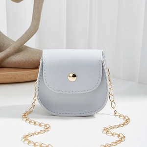Mini light grey crossbody bag with gold chain and circular snap on a minimalist background