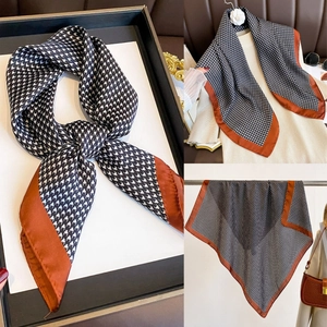 Detailed view of houndstooth silk scarf with burnt orange border tied in a gift box