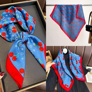 Detail of square silk scarf featuring red cherry patterns and vibrant blue and red contrast