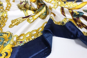 Gros plan d'un foulard en satin avec motifs de chaînes dorées et bordure bleu foncé