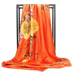 Detail of vibrant orange satin scarf showing large yellow flower prints and silky texture