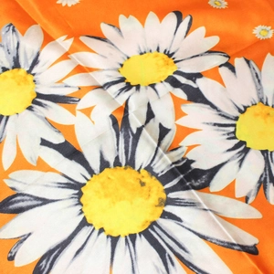 Detail of silk-like satin fabric featuring white daisy print on bright orange background