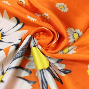 Macro detail of glossy orange satin fabric with white daisy floral pattern and drape
