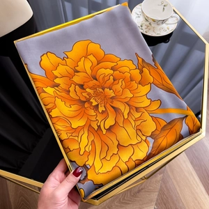 Detailed texture of silver grey floral silk scarf with orange flowers in a gold tray