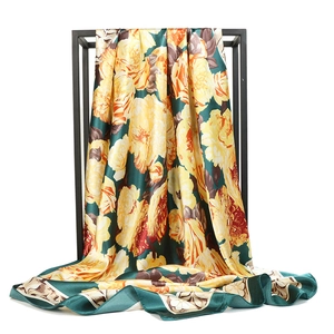 Green satin floral silk scarf with yellow flowers displayed on a black metal rack