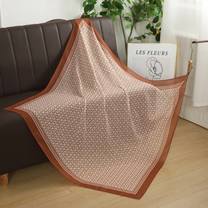 Detail view of a large 110cm square scarf with brown clover pattern on a leather sofa