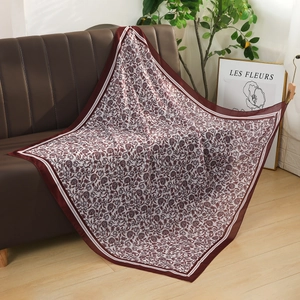 Detailed view of a 110cm square voile floral scarf displayed on a modern brown sofa