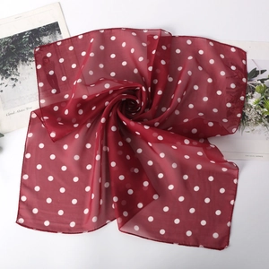 Détail d'un foulard carré en mousseline bordeaux à pois blancs posé sur un magazine chic