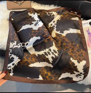 Detail of leopard print silk scarf with brown border styled on a white plush rug