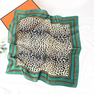 Close-up of leopard print silk scarf with green borders laid on white textured fabric