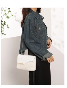 Close-up of white woven shoulder bag featuring a sleek gold chain and elegant metal clasp