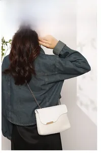 Detailed view of white woven crossbody bag with gold metal trim and chain strap on model